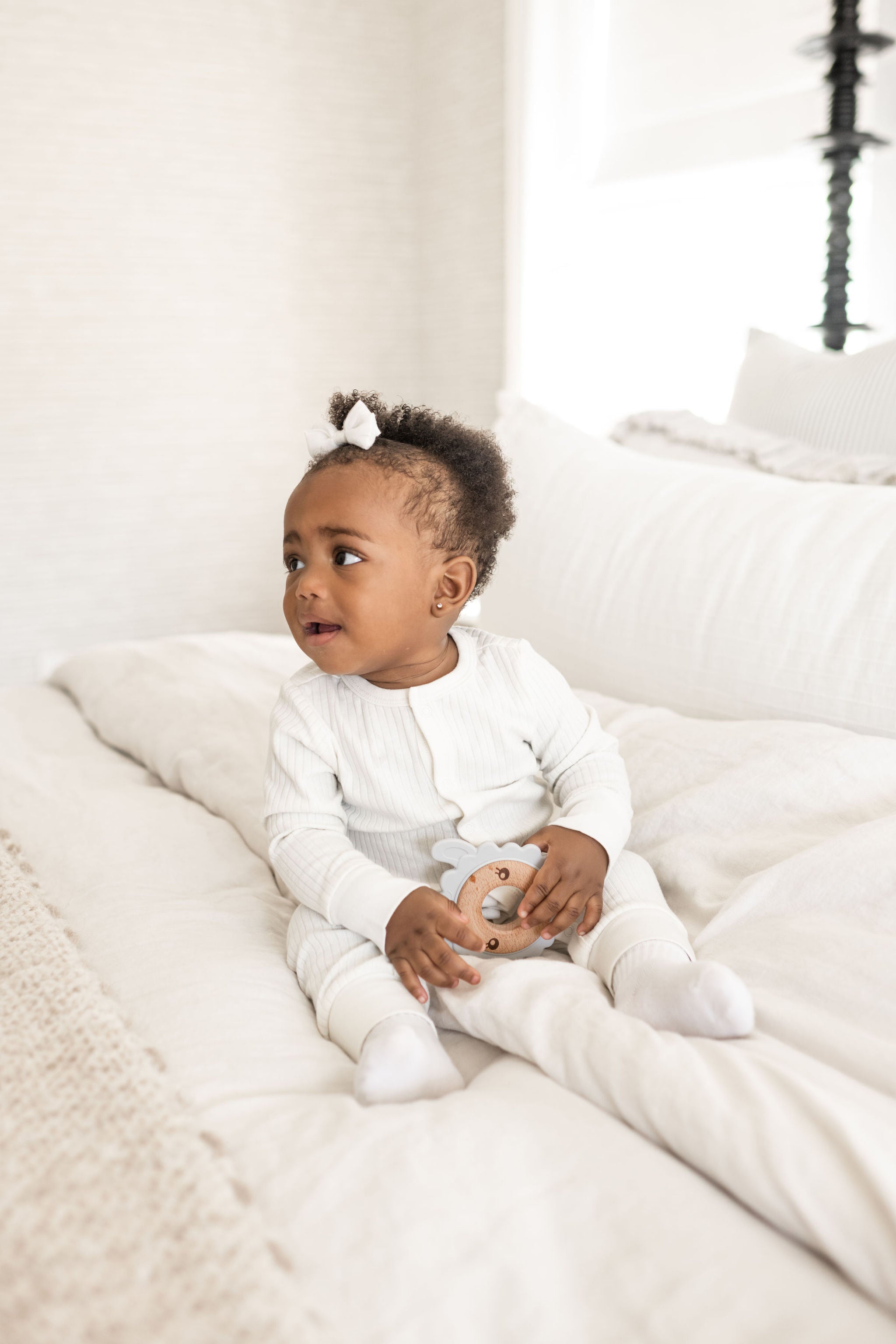 Baby sitting up on bed and holding a Poppyseed Play teether