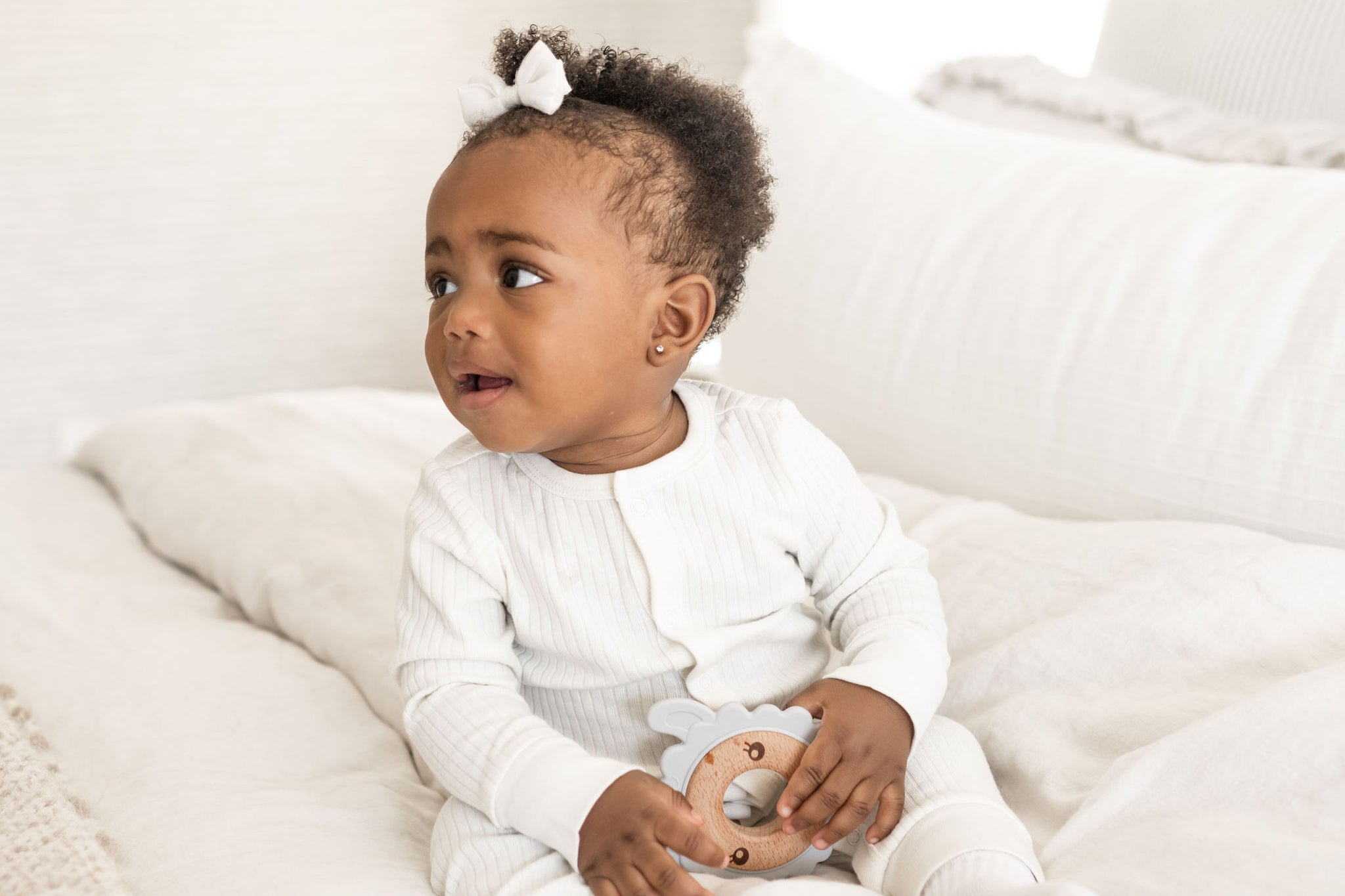 Baby sitting up on bed and holding a Poppyseed Play teether