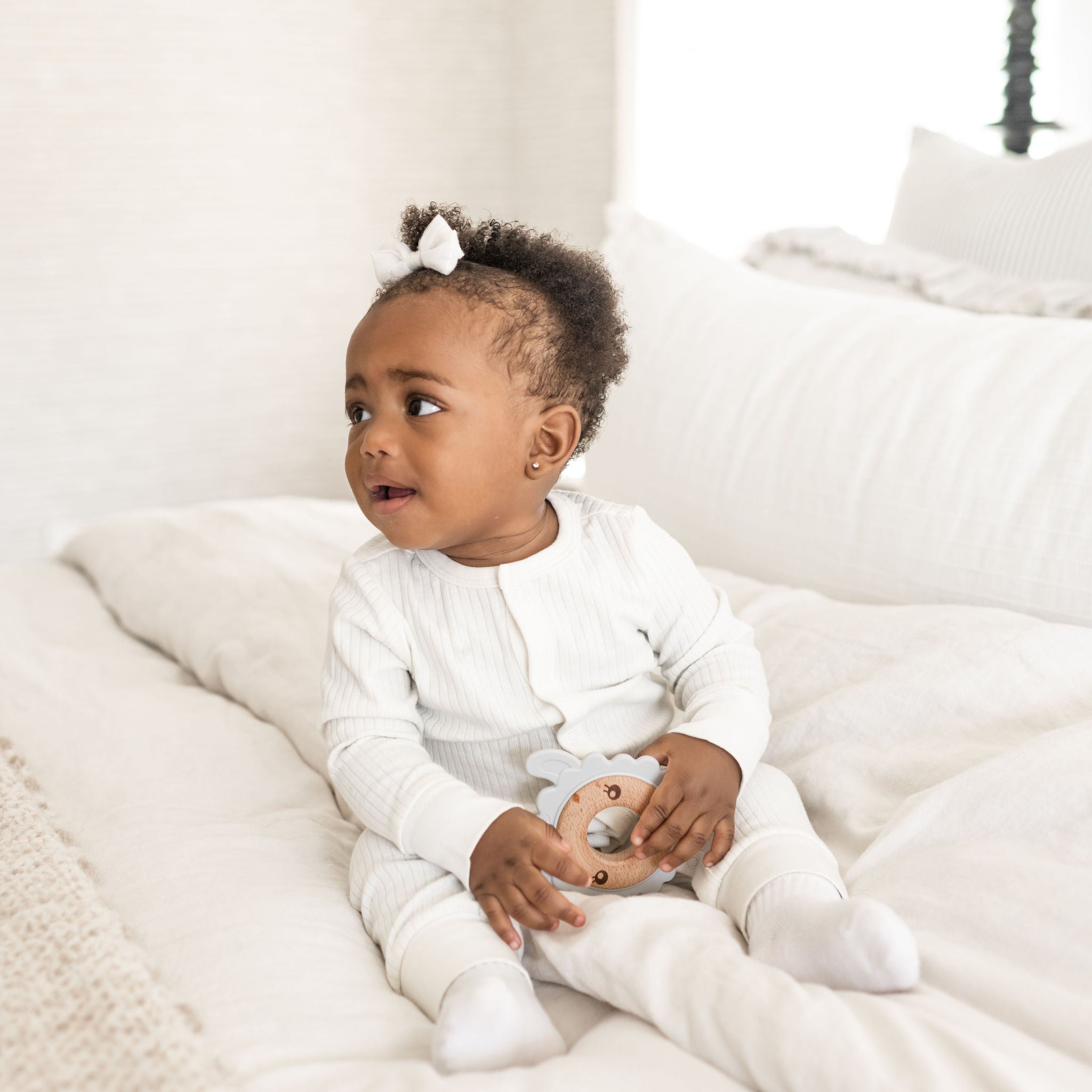 Baby sitting up on bed and holding a Poppyseed Play teether