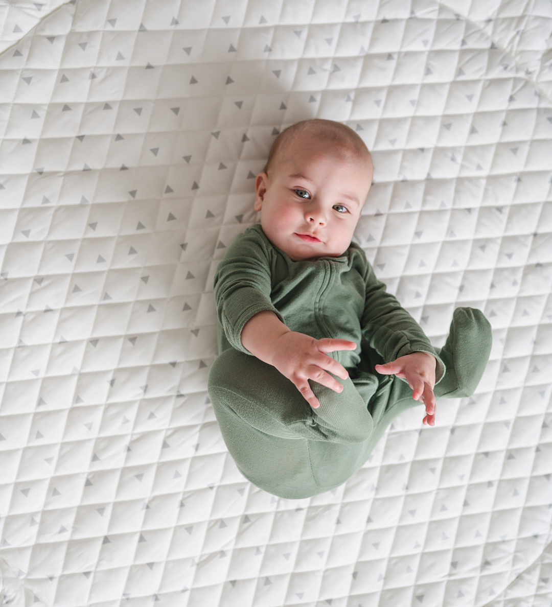 A baby lying on a large, round, beige play mat with a quilted design.
