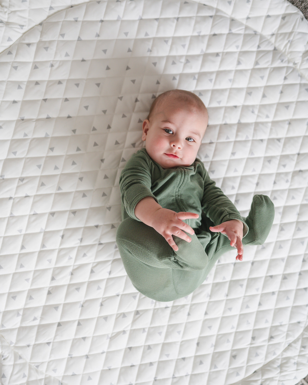 A baby lying on a large, round, beige play mat with a quilted design.