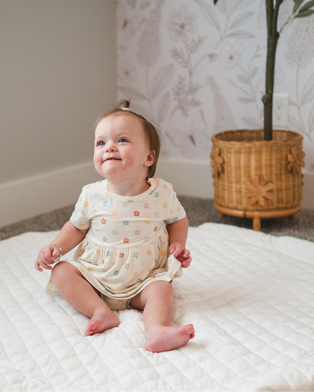 Baby in a floral outfit sitting on the Printed Round Baby Play Mat in a nursery