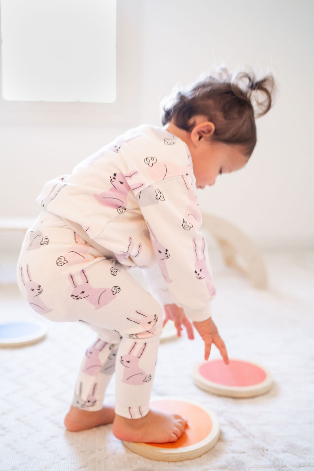 Toddler in bunny pajamas balancing on Wood Stepping Stones on a soft white rug