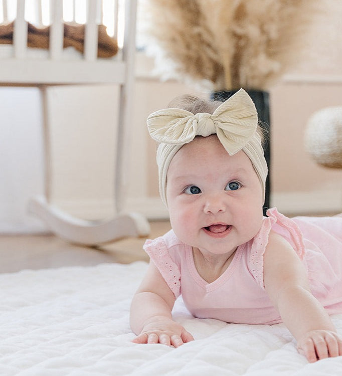 Baby in a pink outfit lying on a white linen infant play mat in a nursery.