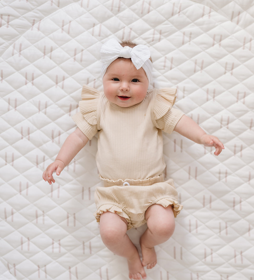 Baby in a cream outfit lying on the Printed Round Baby Play Mat in blush line print