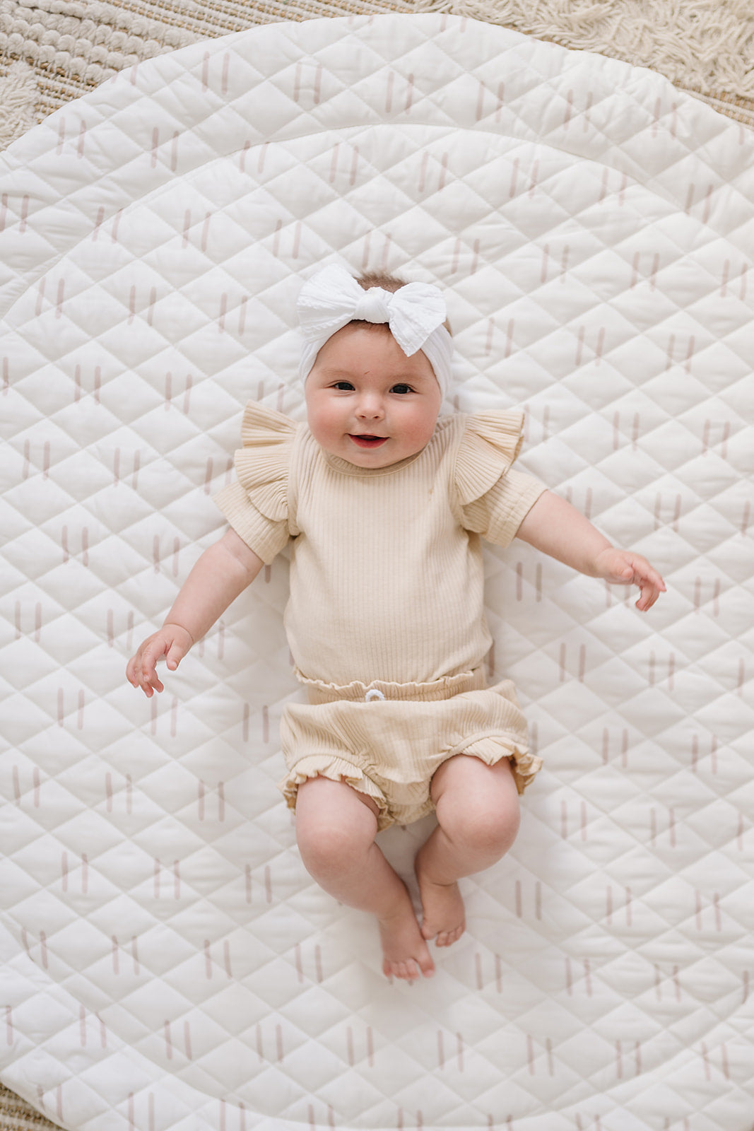 Baby in a cream outfit lying on the Printed Round Baby Play Mat in blush line print