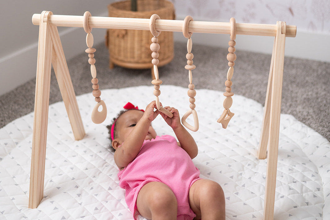 Baby playing with a wooden play gym on a white blanket.