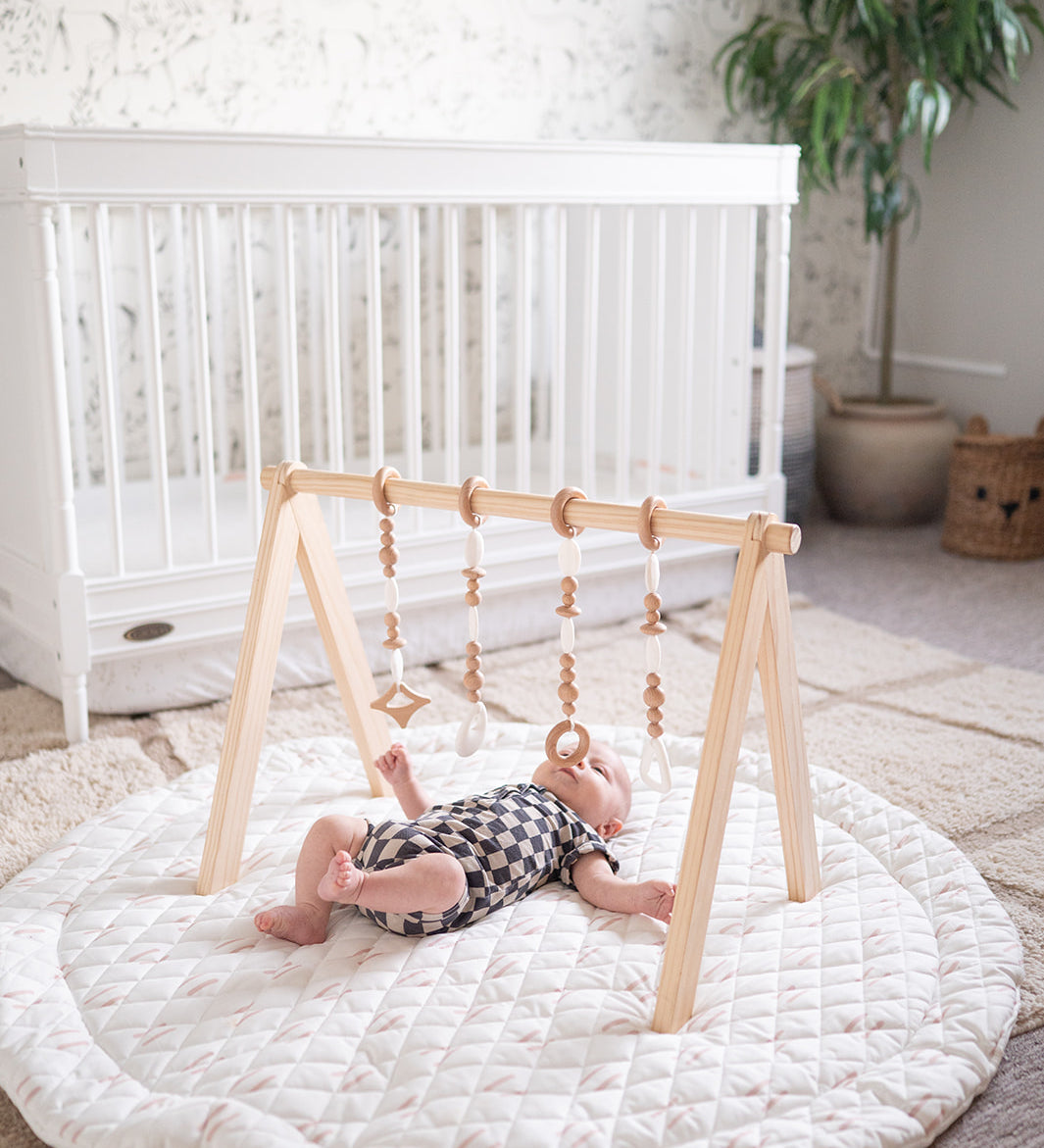 Baby playing on a round white mat with a wooden climbing toy in a nursery.