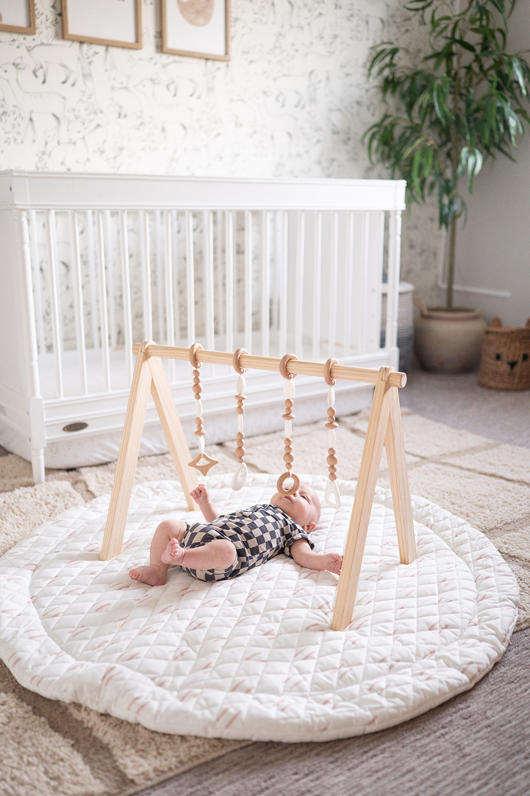 Baby playing on a round white mat with a wooden climbing toy in a nursery.