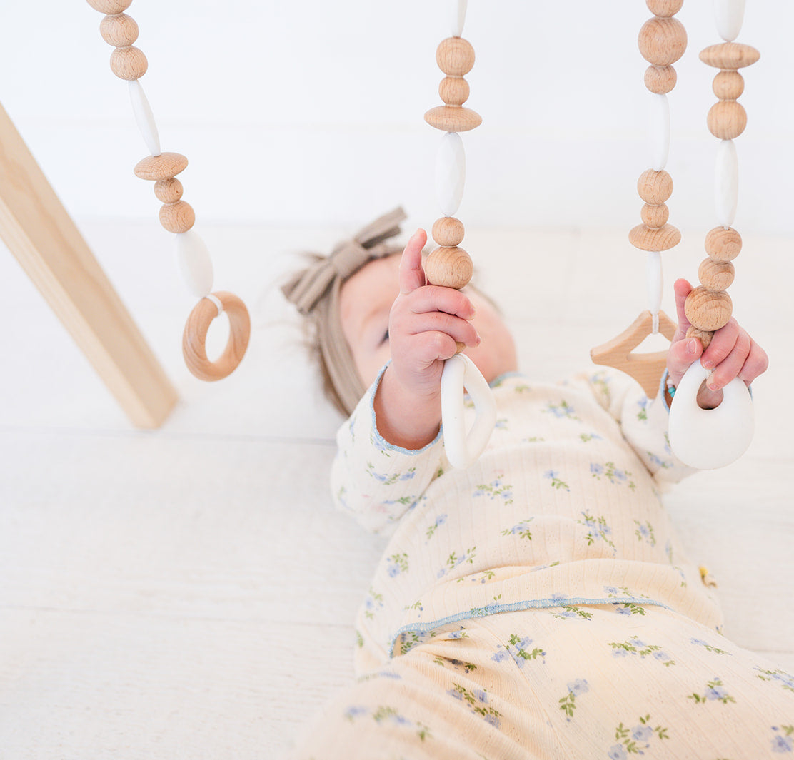 Baby lying on a white blanket with wooden baby toys hanging above