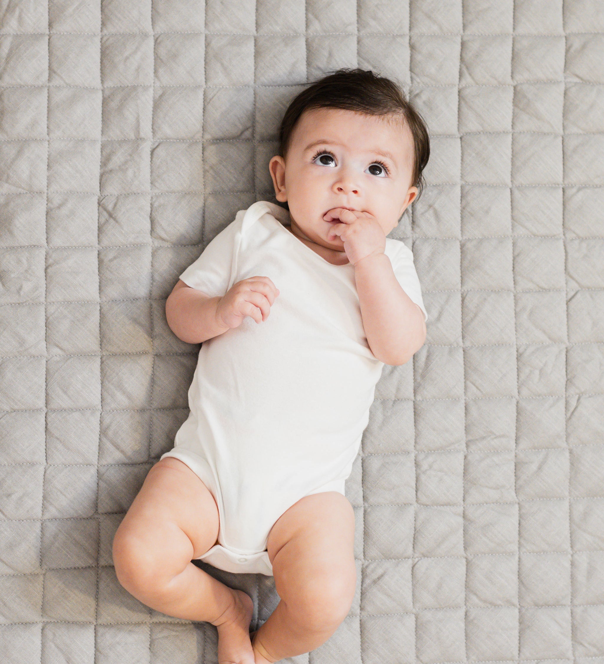 Baby lying on a gray linen infant play mat while looking up.