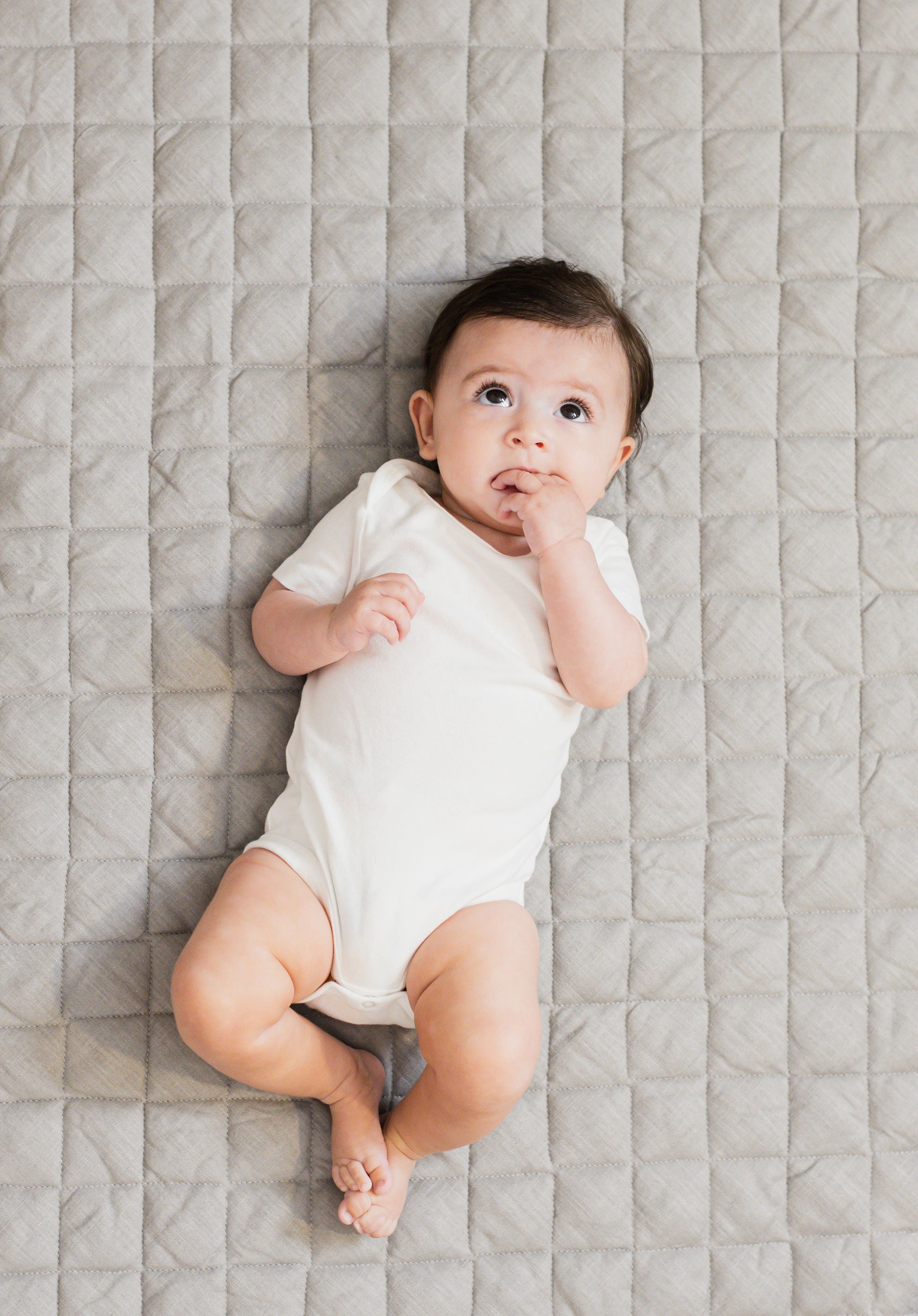 Baby lying on a gray linen infant play mat while looking up.