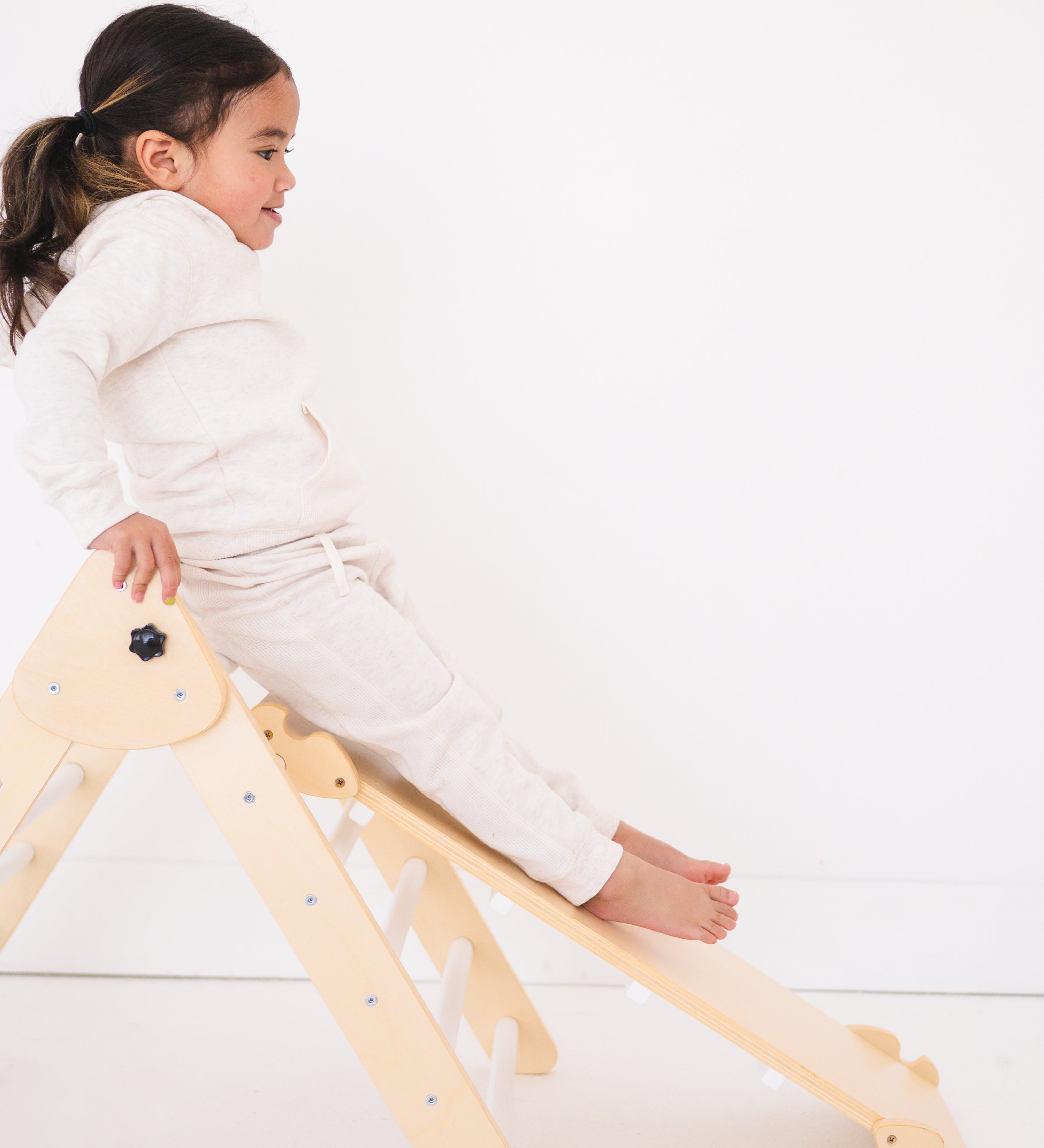 A child sitting on a foldable wooden triangle climber and ramp.