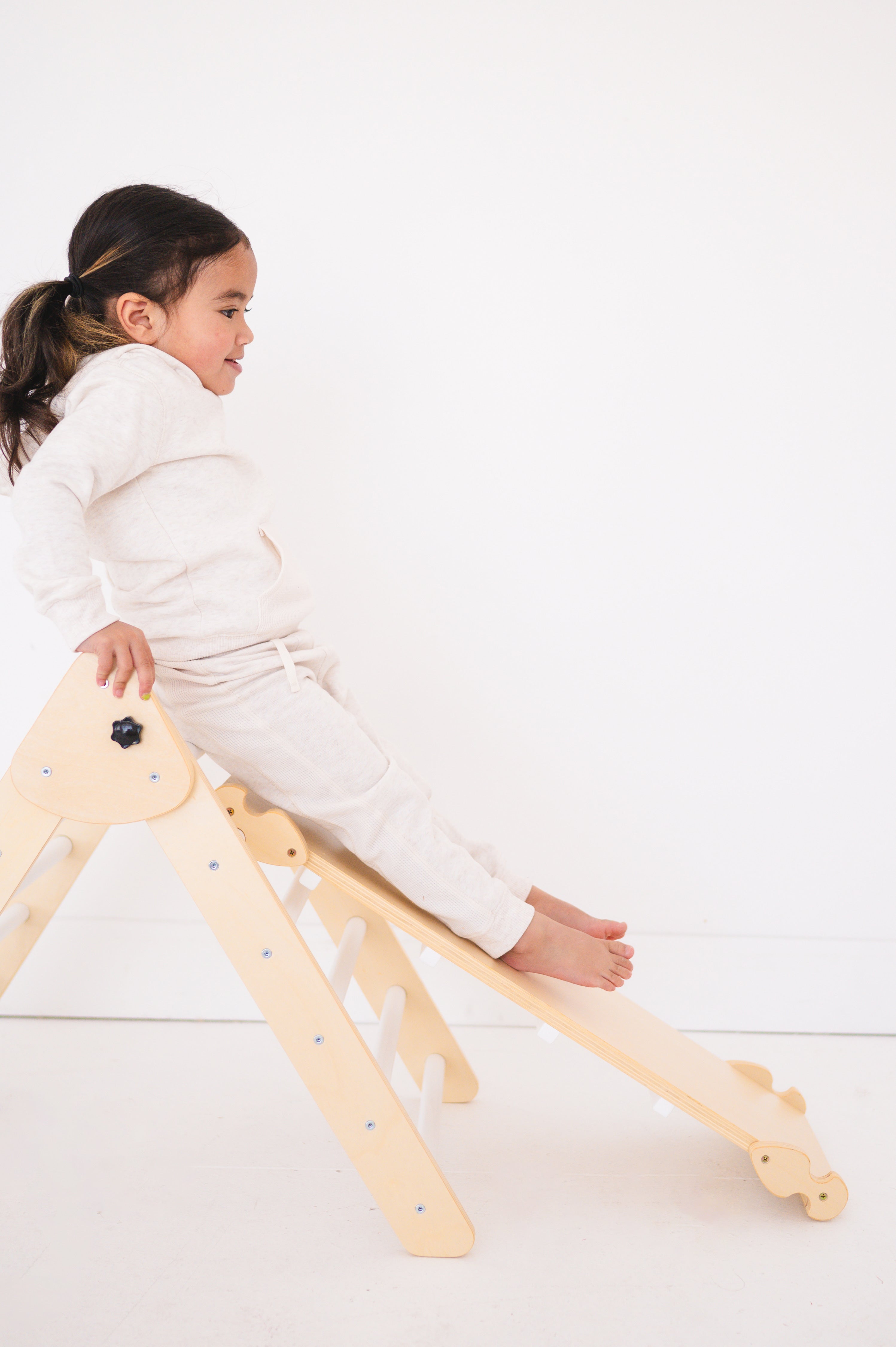 A child sitting on a foldable wooden triangle climber and ramp.