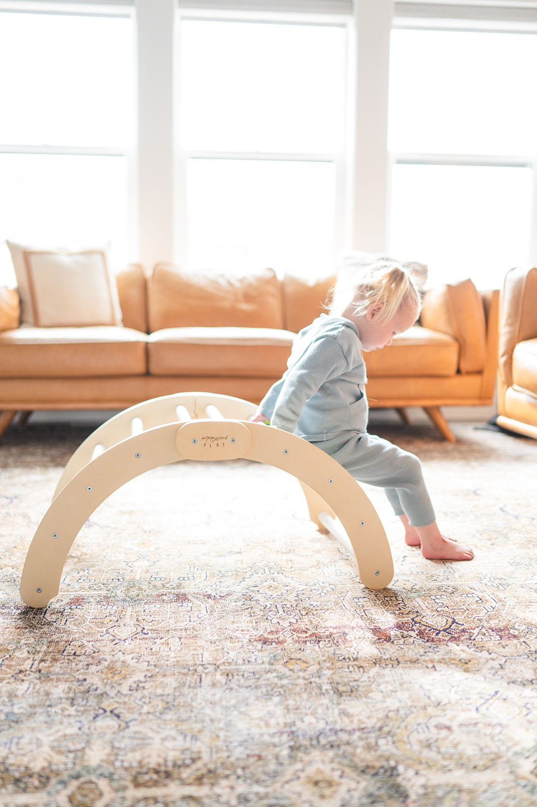 A child playing on a beige wooden climbing arch indoors, with furniture in the background.