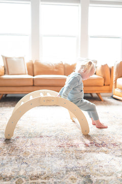 A child playing on a beige wooden climbing arch indoors, with furniture in the background.