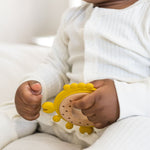 Baby in a white ribbed sleeper holding a yellow silicone & wood teether.