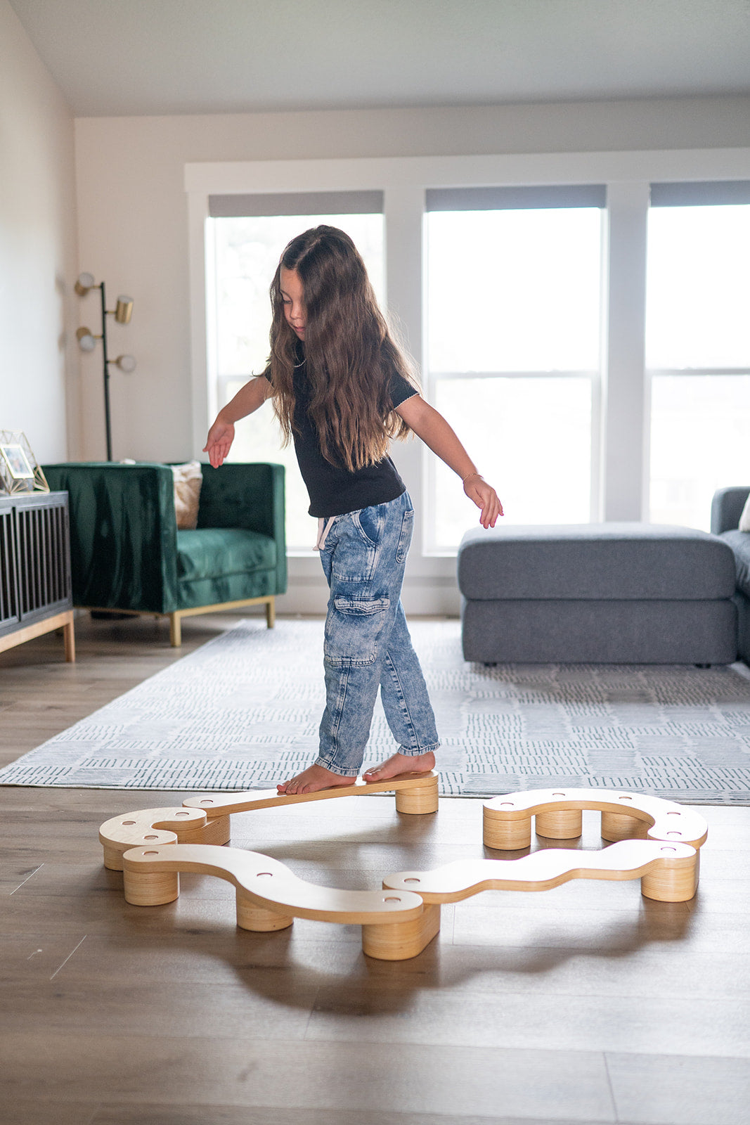Child playing on a wooden balance beam in a living room.