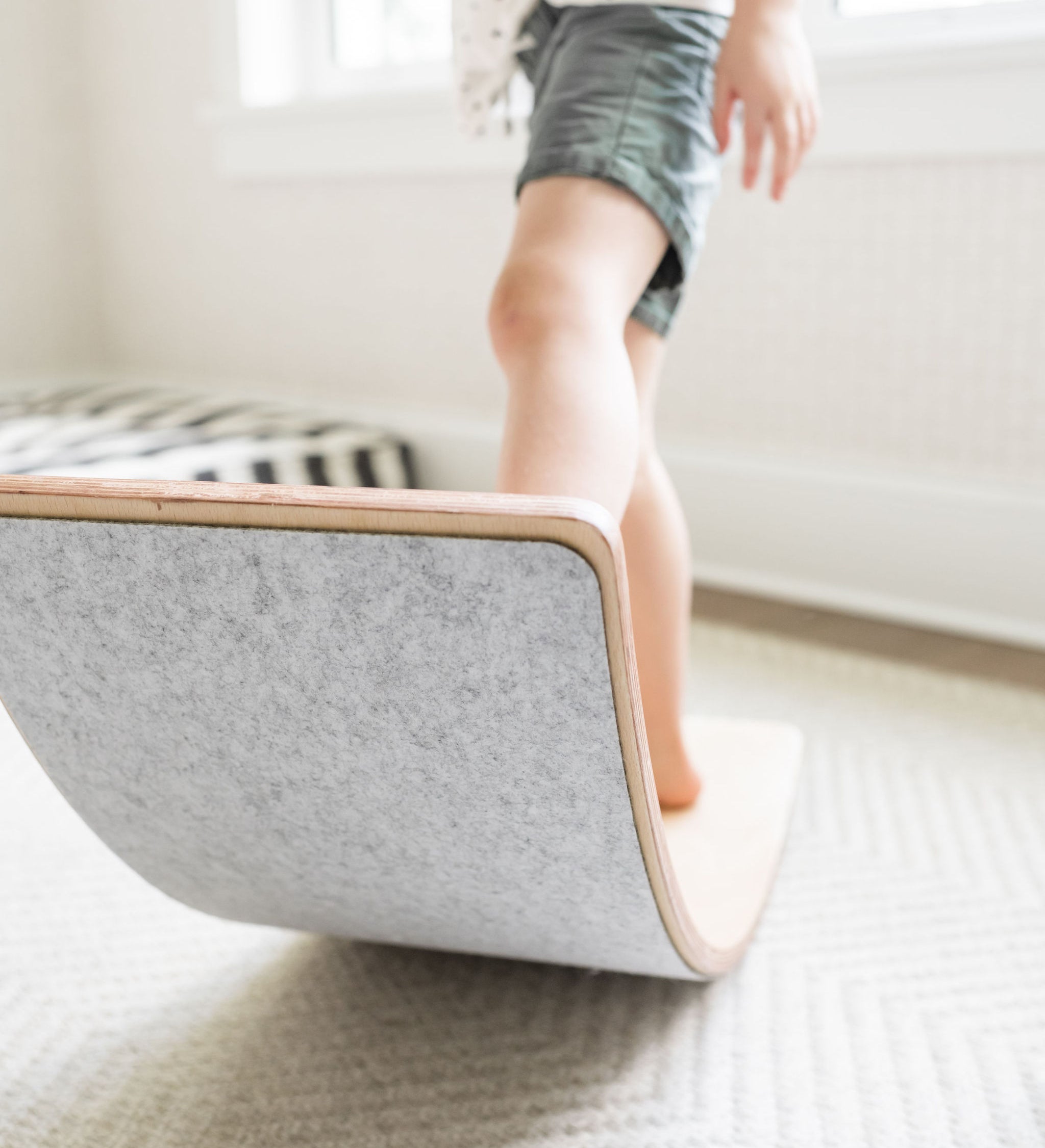 Young child balancing on a Poppyseed Play wooden balance board in a bright room.
