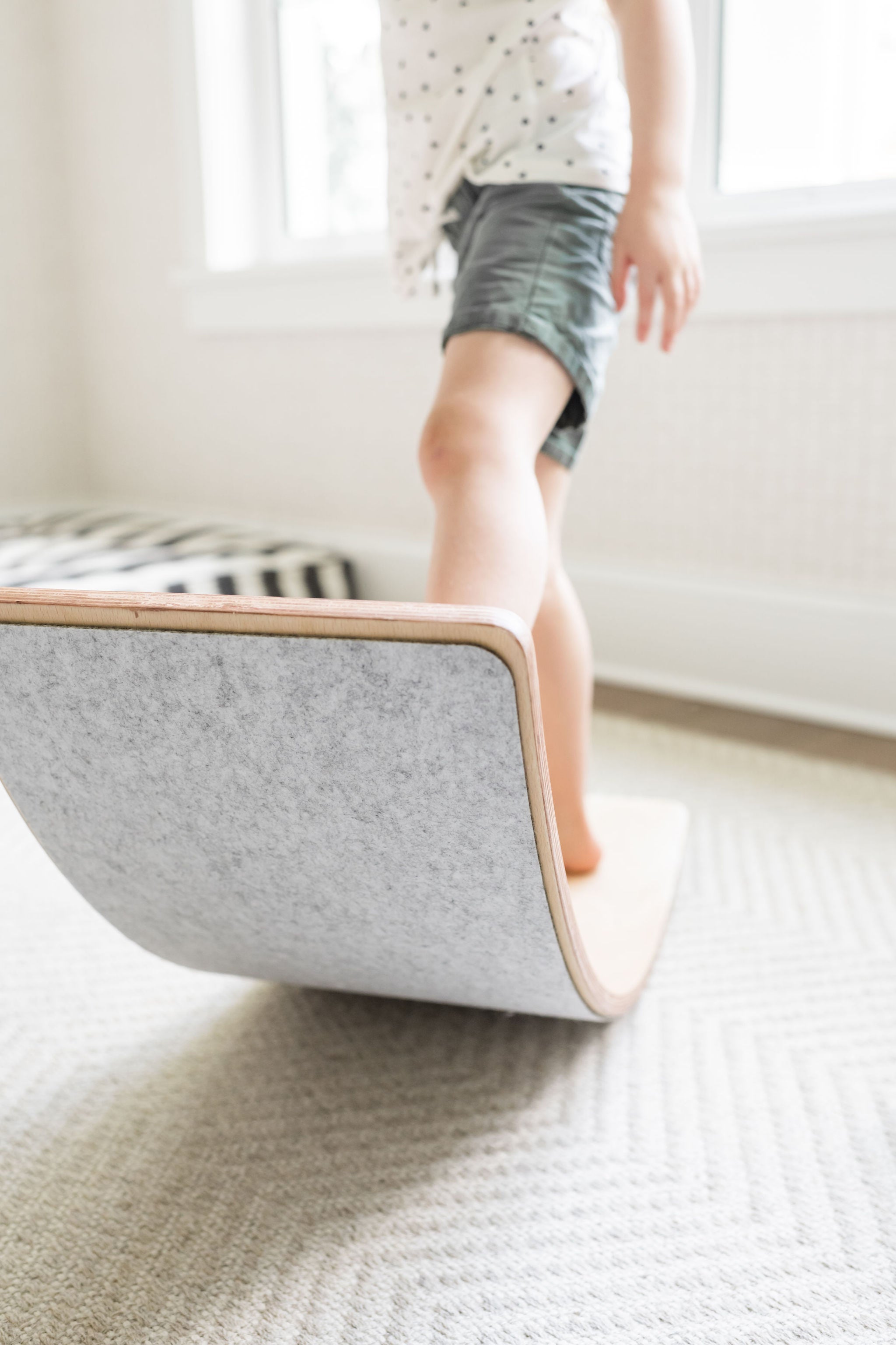 Young child balancing on a Poppyseed Play wooden balance board in a bright room.
