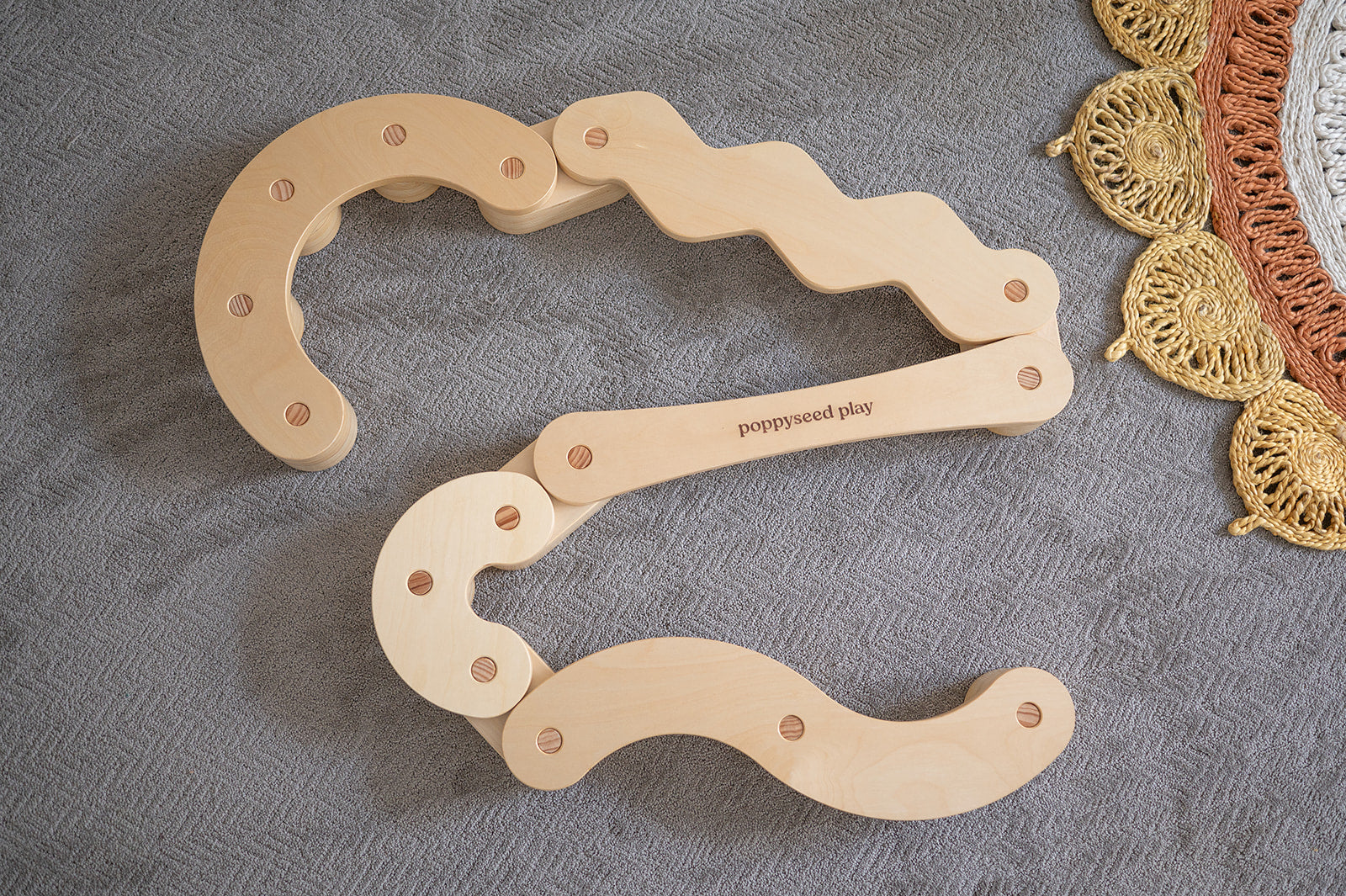 Wooden toy with wavy design on a textured surface, featuring 'poppywood play' branding.