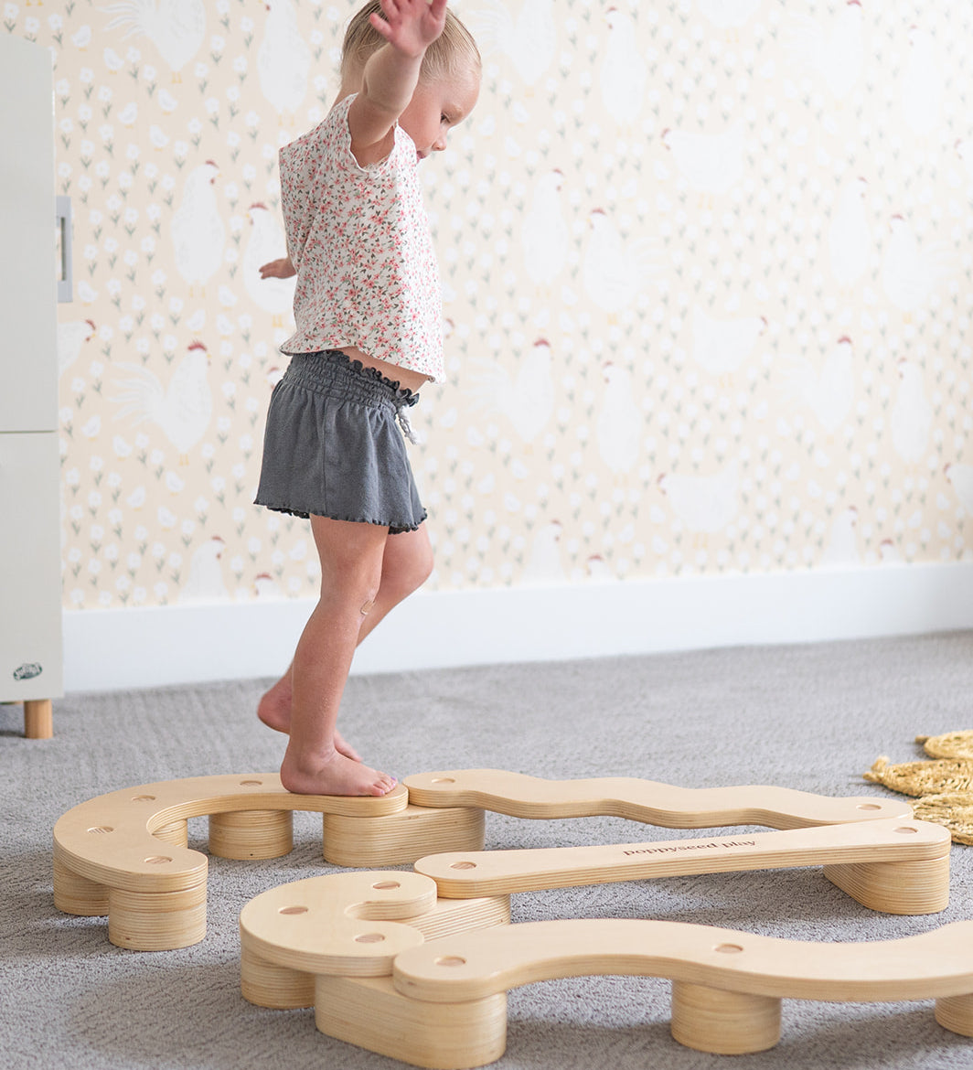 Child playing with a wooden balance beam on a carpeted floor.