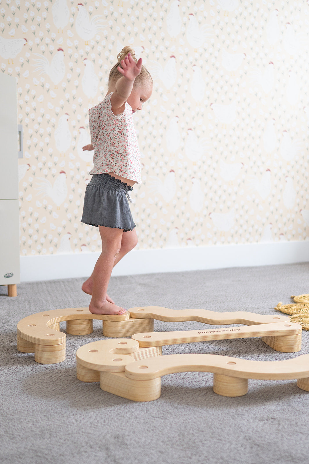 Child playing with a wooden balance beam on a carpeted floor.