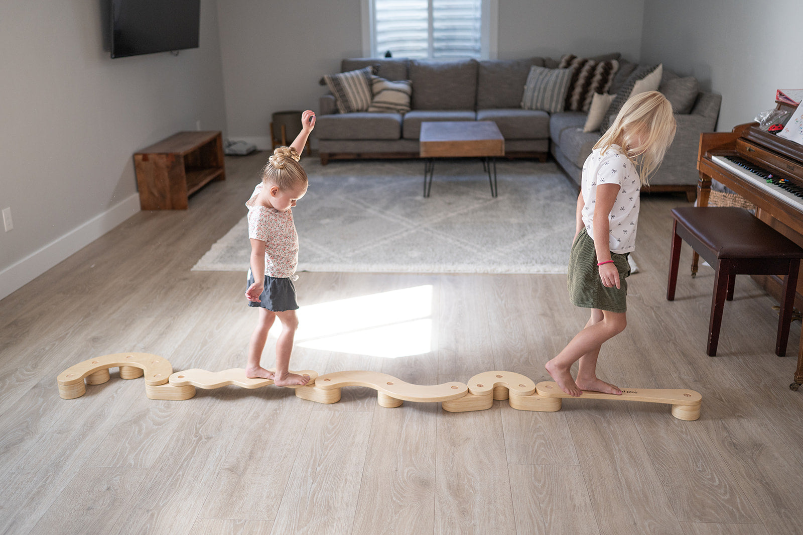 Two children playing with a wooden balance beam in a living room.