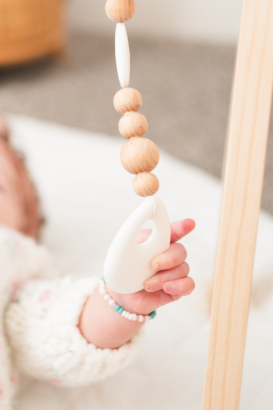 Baby hand holding a wooden teething ring with beads
