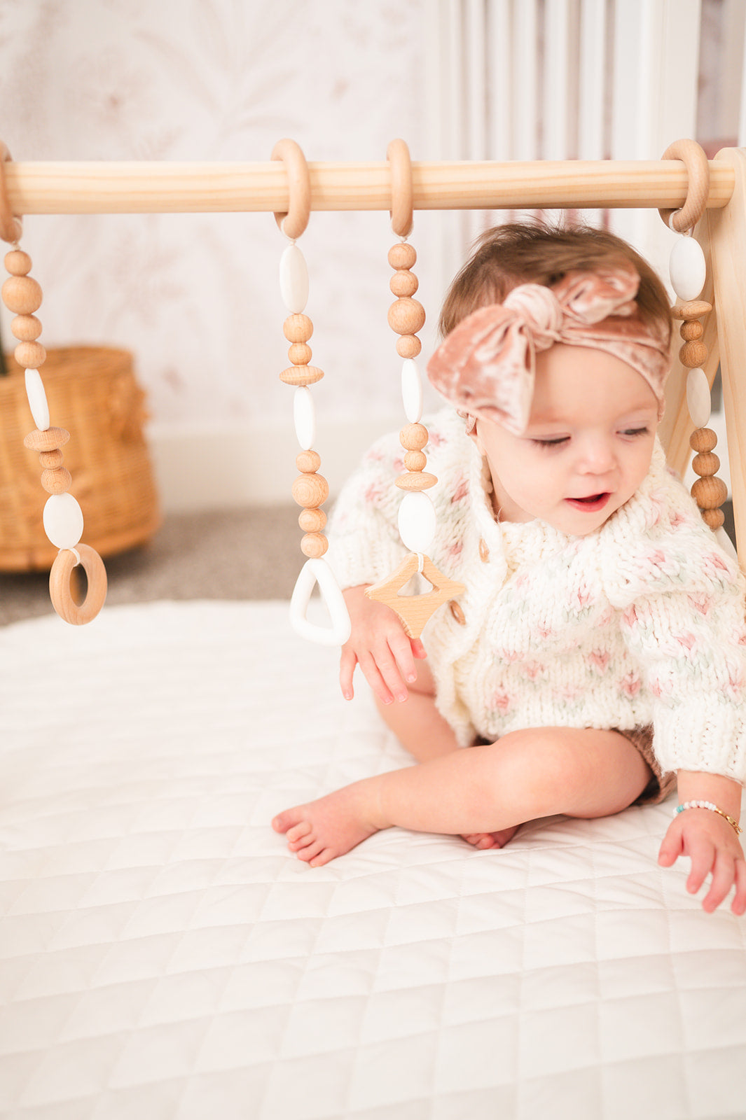 Baby sitting on a bed with a wooden bead gym in the background
