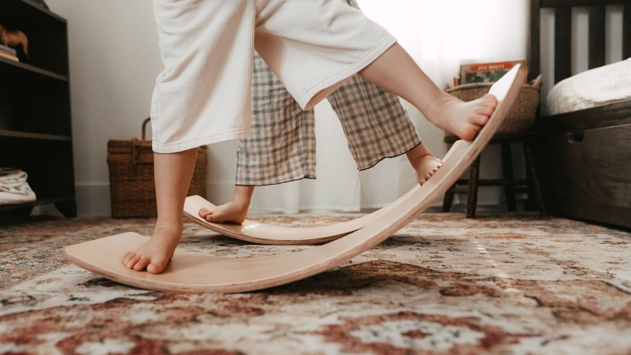 Young child balancing on a Balance Board Bundle over a patterned rug in a bedroom.