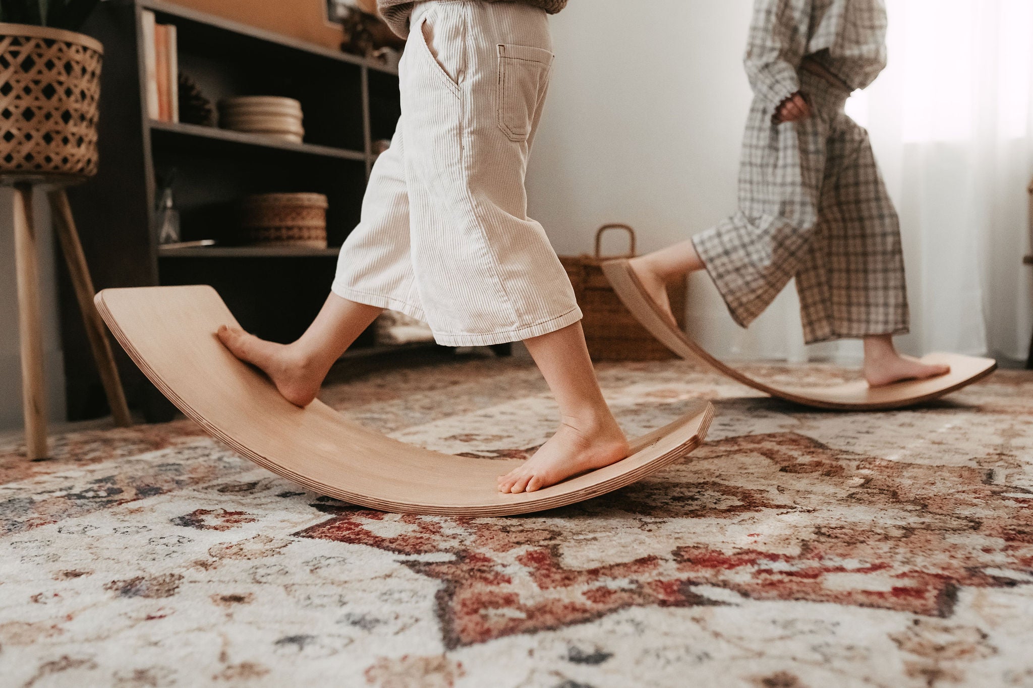Two children balancing on wooden balance boards in a room with a patterned carpet.