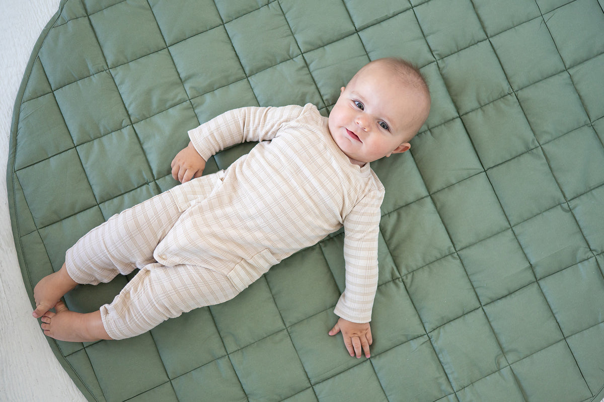 Baby stretched out on the olive Neutral Round Baby Play Mat