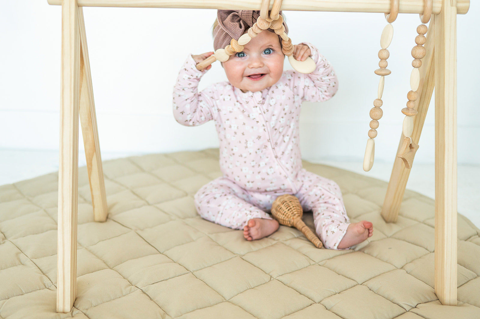 Smiling baby playing under a wooden baby gym on the taupe Neutral Round Baby Play Mat