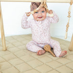 Smiling baby playing under a wooden baby gym on the taupe Neutral Round Baby Play Mat